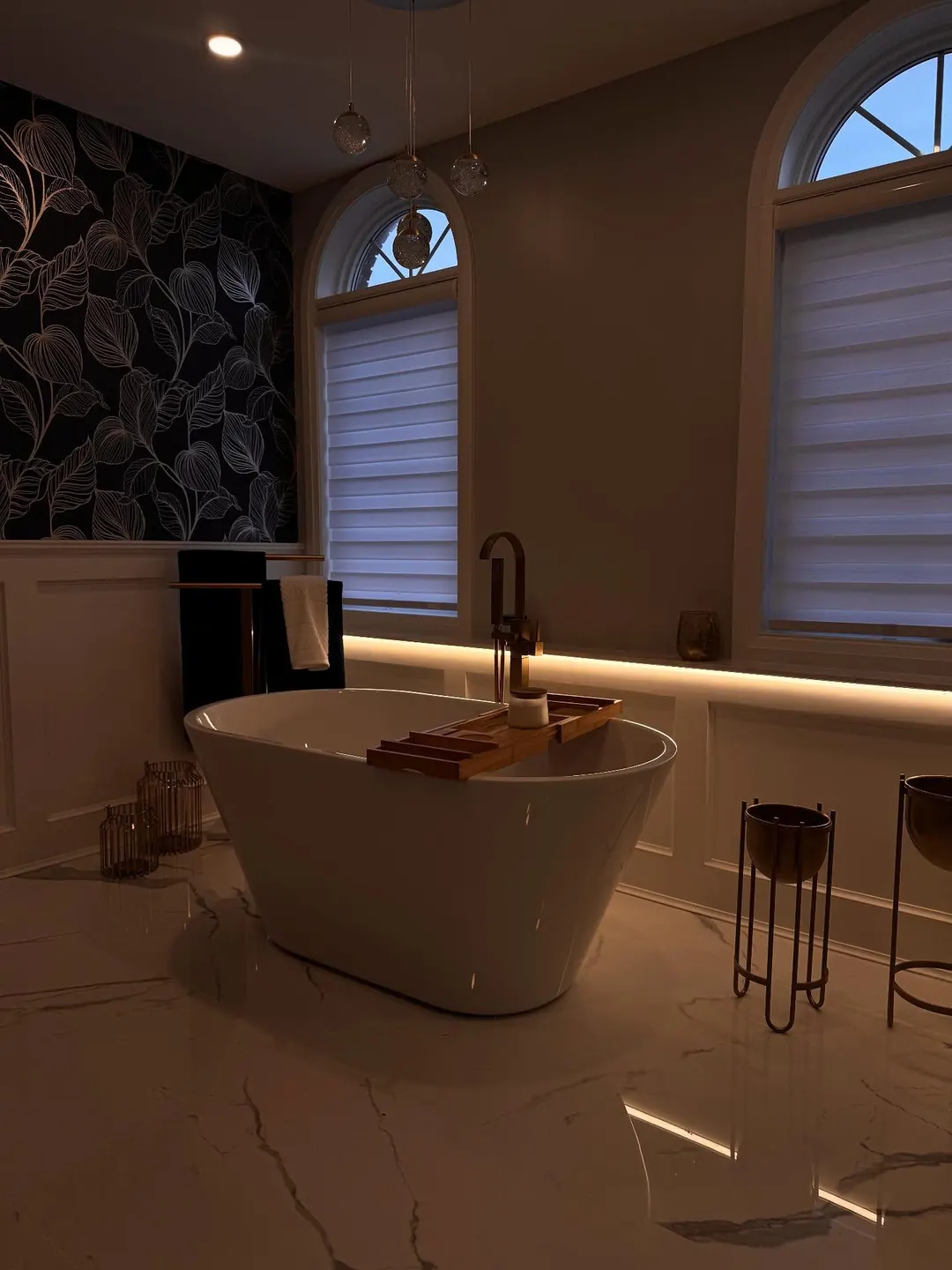 Freestanding bath beneath arched windows with warm concealed lighting.