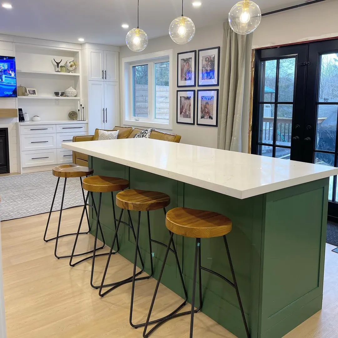 Kitchen with a deep green island, stone worktop and brass-toned stools.