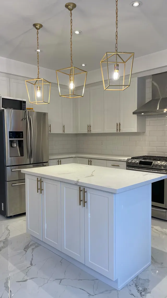 White kitchen with brass pendant lighting over a stone island.